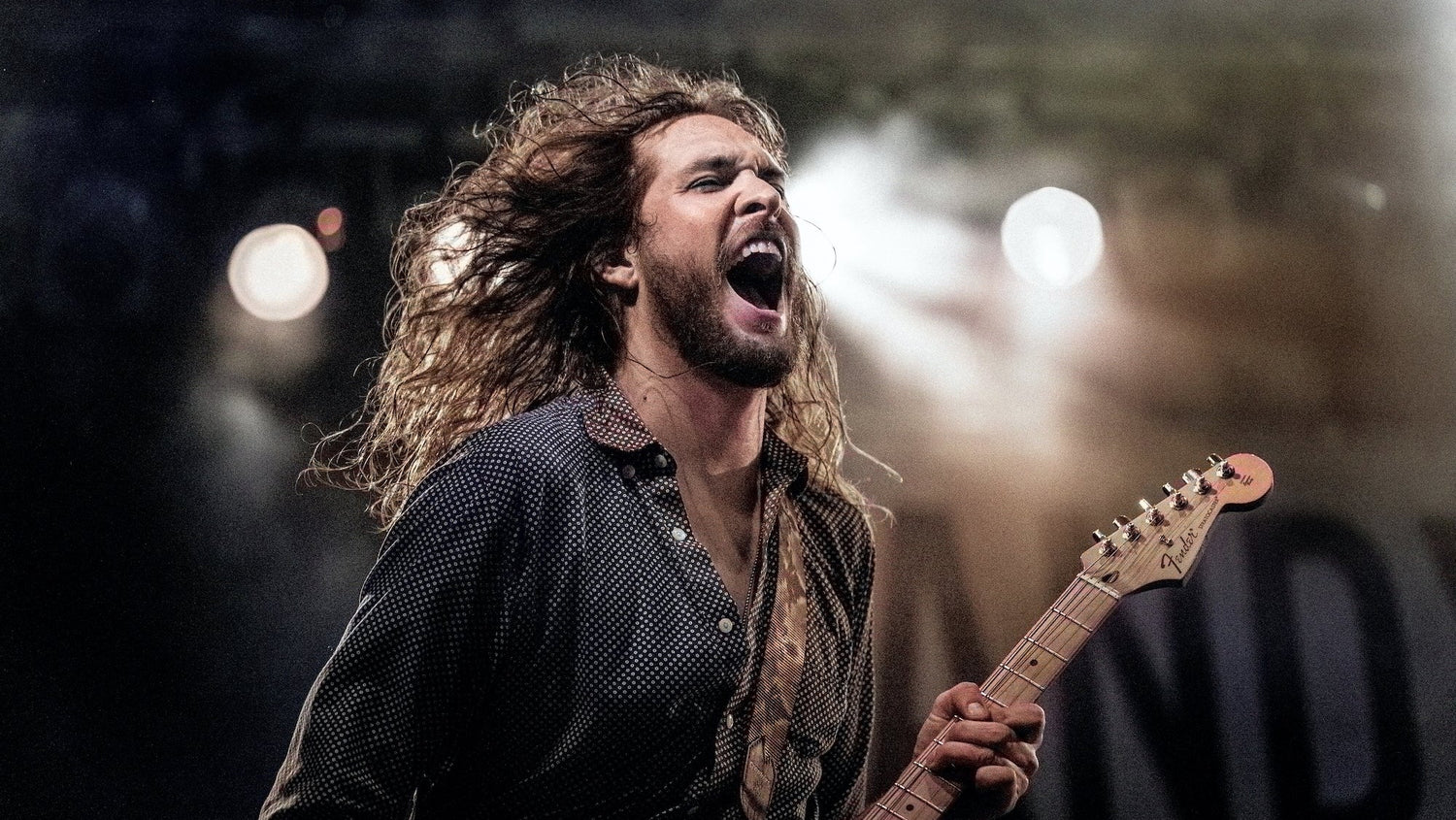 Man with long hair playing guitar on stage with a blurred background